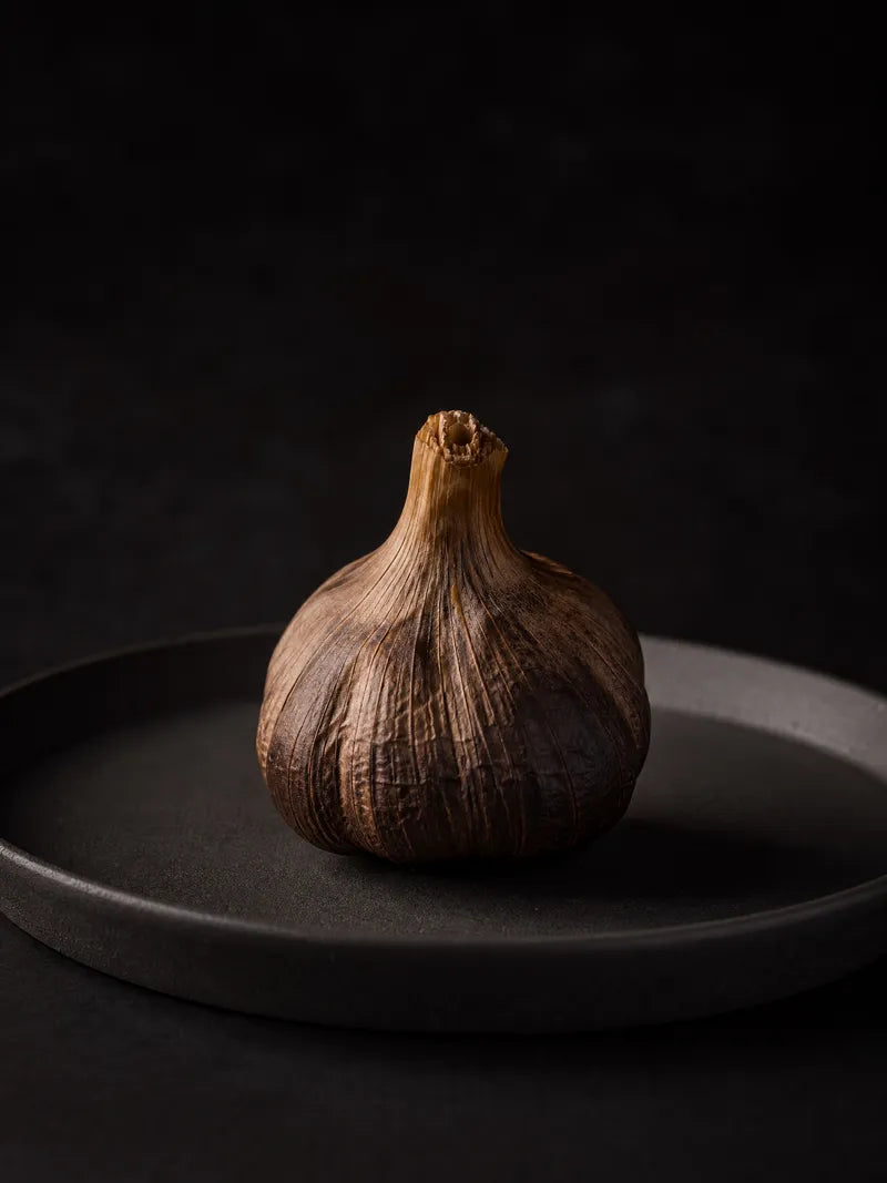 A pristine black garlic bulb on a dark ceramic plate